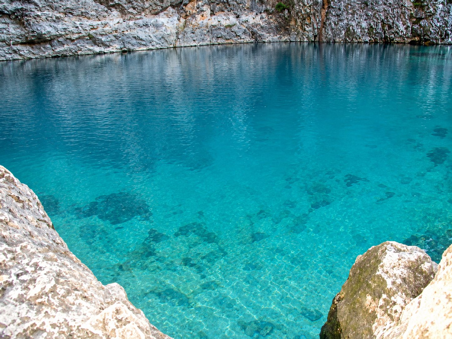 Eau turquoise de la Fontaine de Vaucluse entre des rochers clairs.