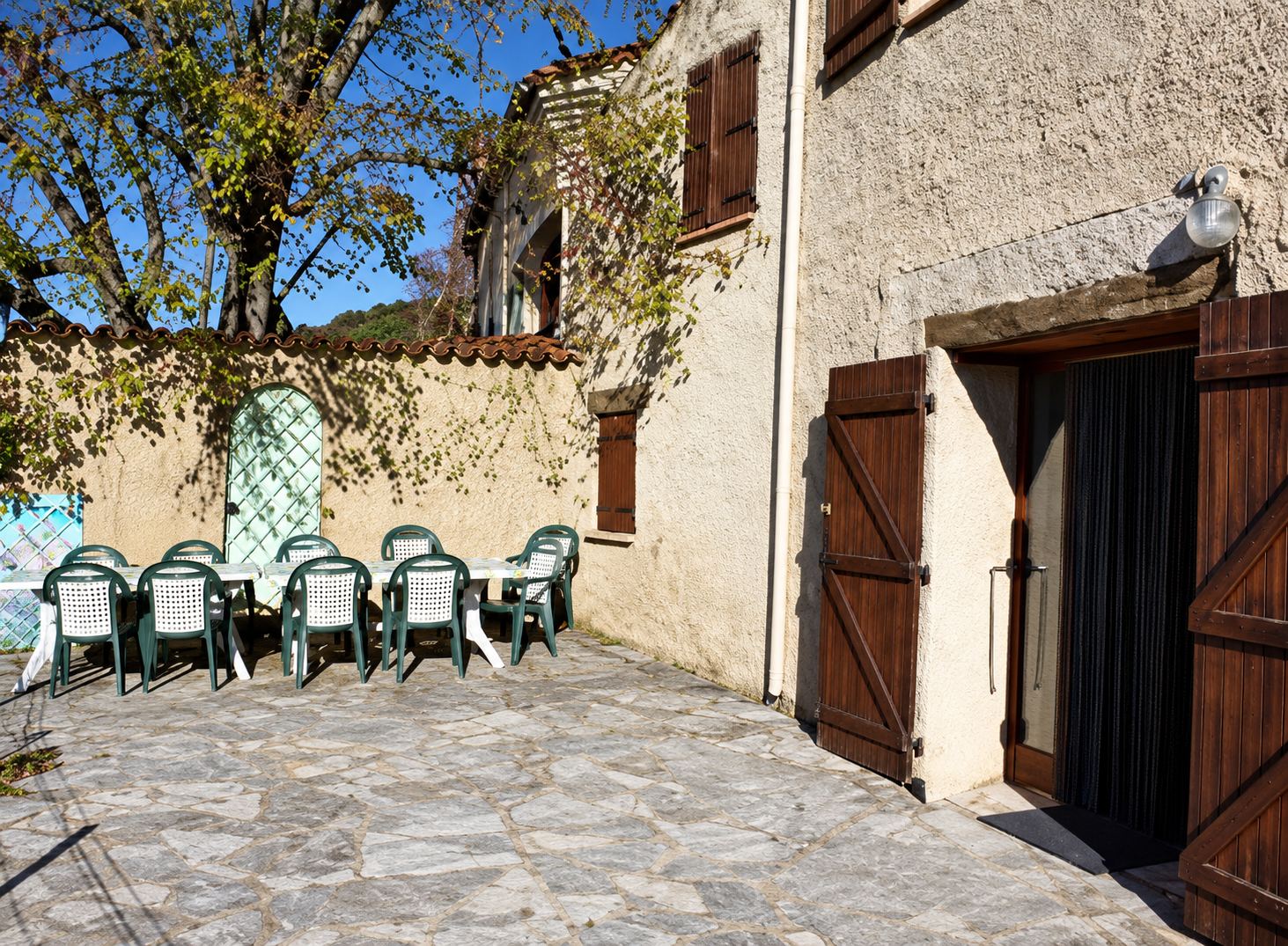 Terrasse dallée du gîte Tilleul avec chaises, façade en pierre et portes en bois.